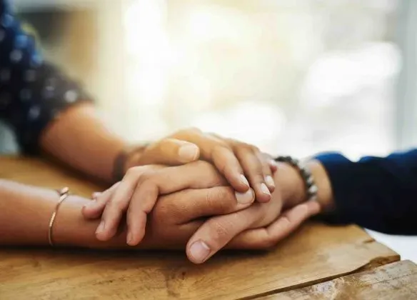Gros plan sur deux mains qui se tiennent sur une table en bois en signe de soutien.