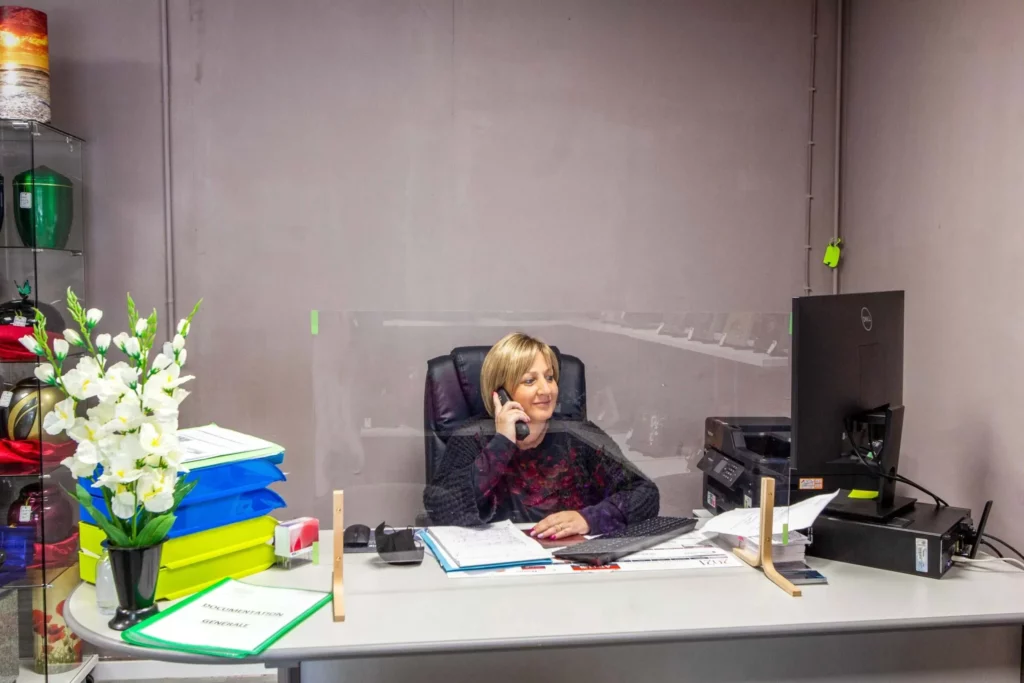 Conseillère funéraire au téléphone derrière une vitre de protection plexiglas au bureau.