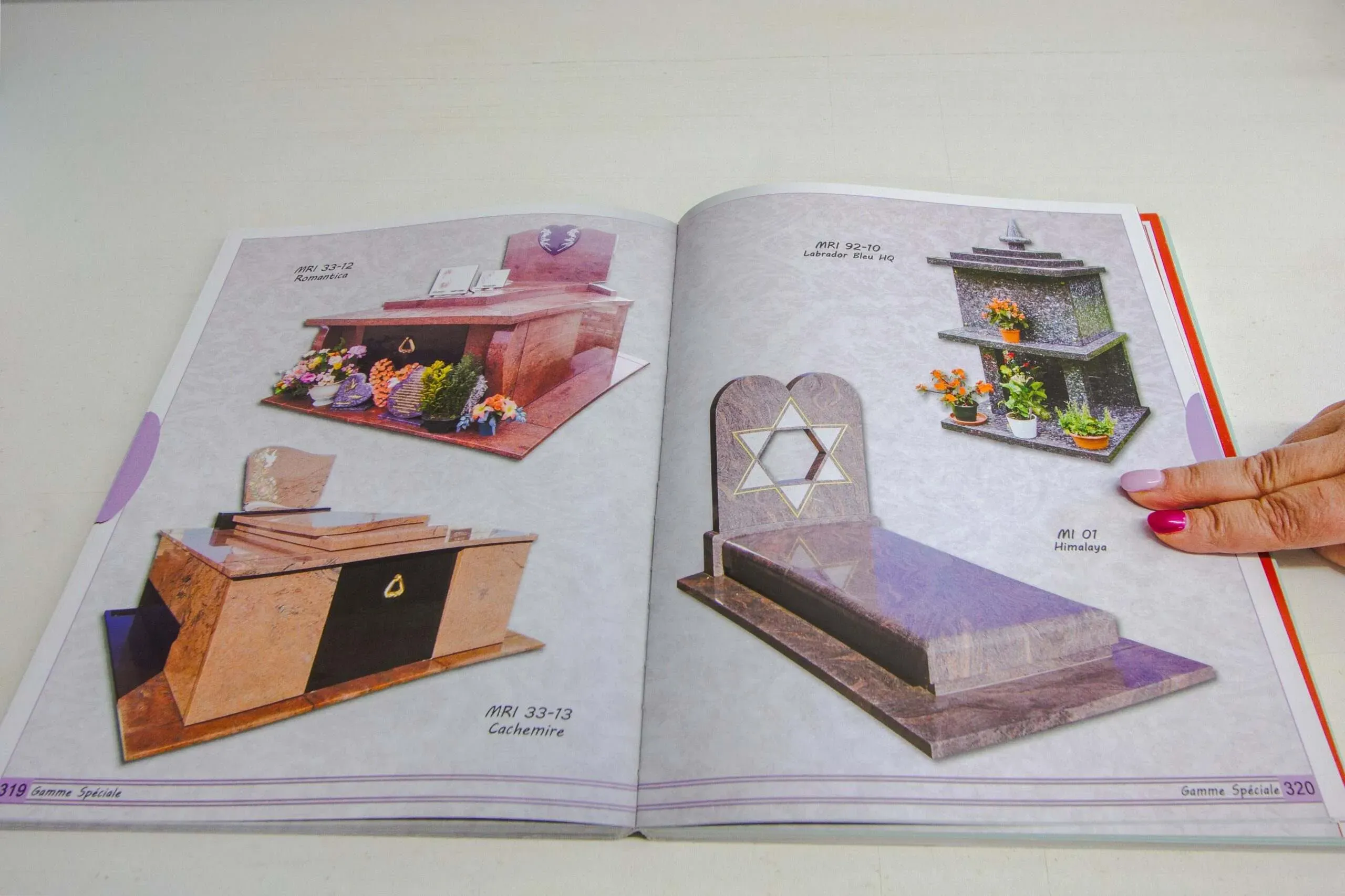 Une main feuillette un catalogue papier de monuments funéraires et pierres tombales.